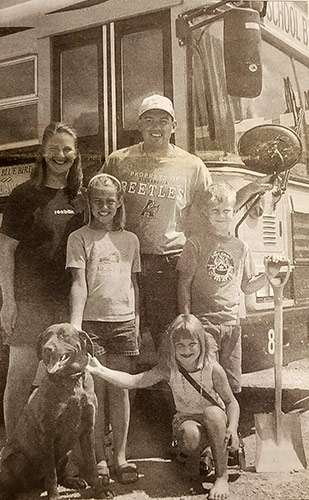 Mike and Jenny Aksmit with their three kids and family dog posing for a photo next to one of their school buses