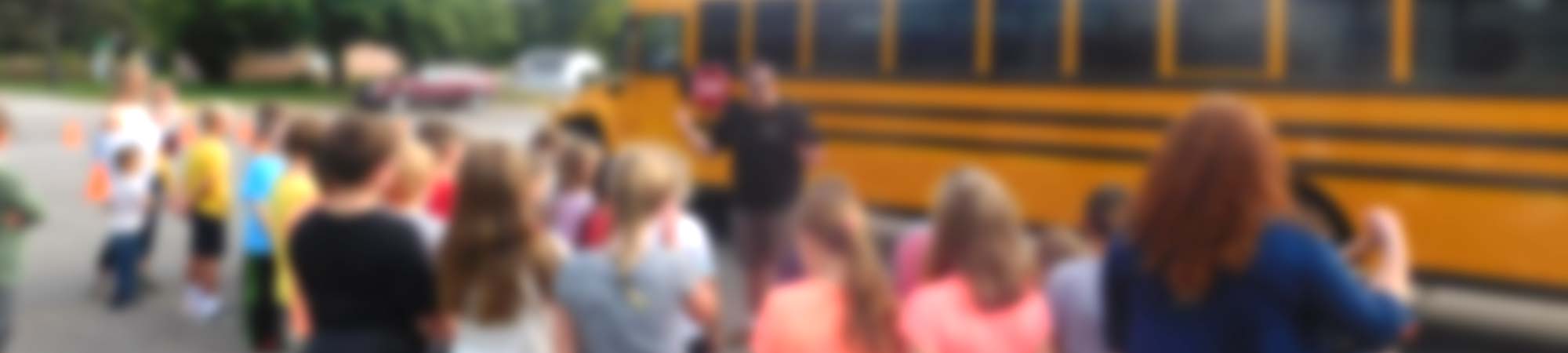 Blurred photo of an Aksamit bus driver performing a school bus safety class with a group of children